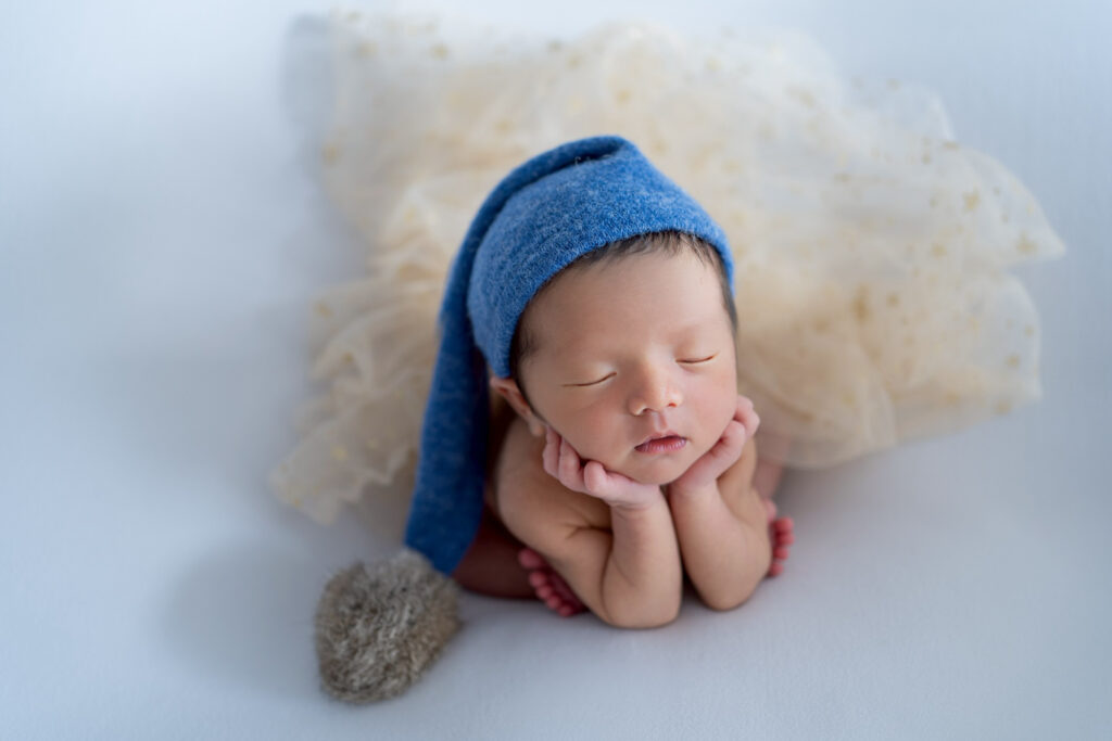 青いニット帽をかぶり、頬づえのポーズで眠る新生児。2枚を合成したニューボーンフォト